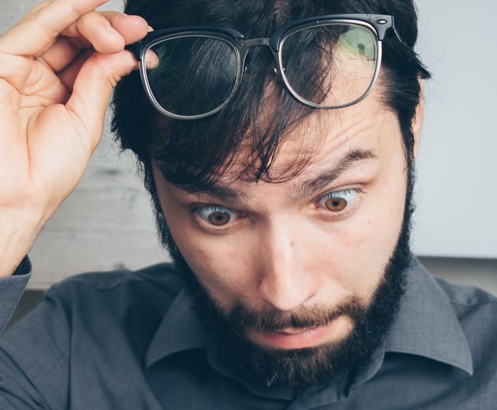 A man with eyeglasses looks surprised while reading. His expression shows shock and disbelief.